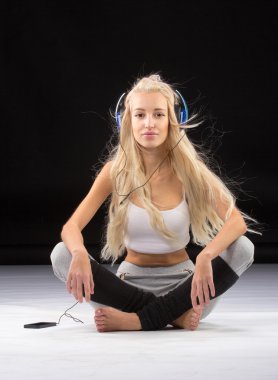 Gülümseyen kadın yerde kulaklıklarıyla oturuyor.