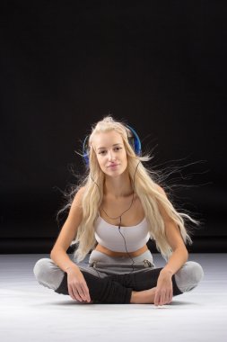 Gülümseyen kadın yerde kulaklıklarıyla oturuyor.