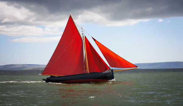 Traditional wooden boat with red sail.