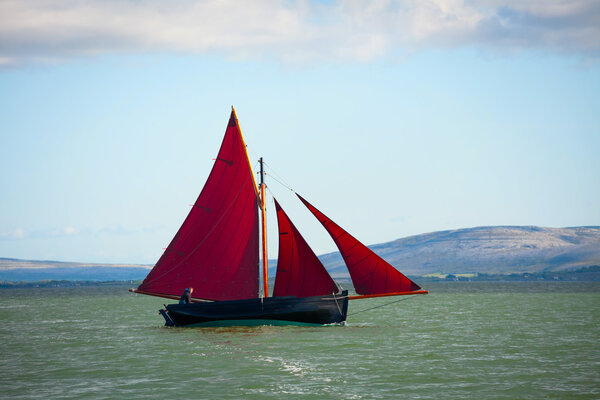 Traditional wooden boat with red sail.