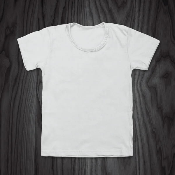 White blank t-shirt on dark wood desk — Stock Photo, Image