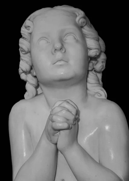 Boy statue pray to God with hands held together. Beautiful old stone statue of praying child isolated on black background