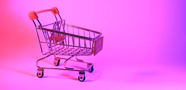 Carro de compras con luz de neón de moda. Gradiente rosa-azul resplandor. Arte conceptual. Retro 80. Concepto de compras minimalista. Carro de compras de juguete, neón —  Fotos de Stock