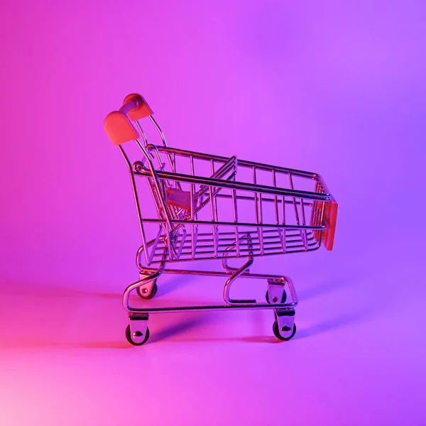 Nakupování s vozíkem v módním neonovém světle. Zářivě růžově modrá záře. Koncept umění. Retro 80s. Minimalistický koncept nakupování. Nákupní vozík, neon — Stock fotografie