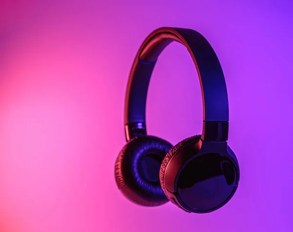 Stylish black wireless headphones lit with colorful neon light on abstract background isolated. Modern technology concept with copy space — Stock Photo, Image