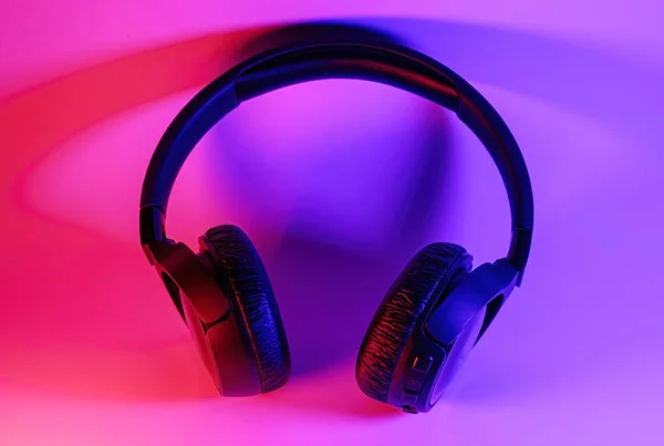 Fones de ouvido sem fio pretos elegantes iluminados com luz de néon colorida no fundo abstrato isolado. Conceito de tecnologia moderna com espaço de cópia — Fotografia de Stock