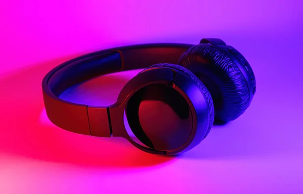 Elegantes auriculares inalámbricos negros iluminados con luz de neón colorida sobre fondo abstracto aislado. Concepto de tecnología moderna con espacio de copia — Foto de Stock