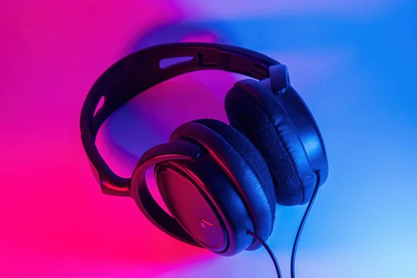 Stylish black wireless headphones lit with colorful neon light on abstract background isolated. Modern technology concept with copy space — Stock Photo, Image