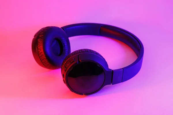 Elegantes auriculares inalámbricos negros iluminados con luz de neón colorida sobre fondo abstracto aislado. Concepto de tecnología moderna con espacio de copia — Foto de Stock