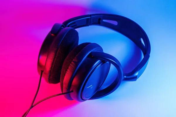 Stijlvolle zwarte draadloze hoofdtelefoon verlicht met kleurrijk neon licht op abstracte achtergrond geïsoleerd. Modern technologieconcept met kopieerruimte — Stockfoto