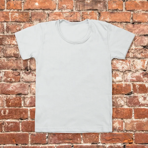 Szary t-shirt puste na tle ciemnej cegły — Zdjęcie stockowe