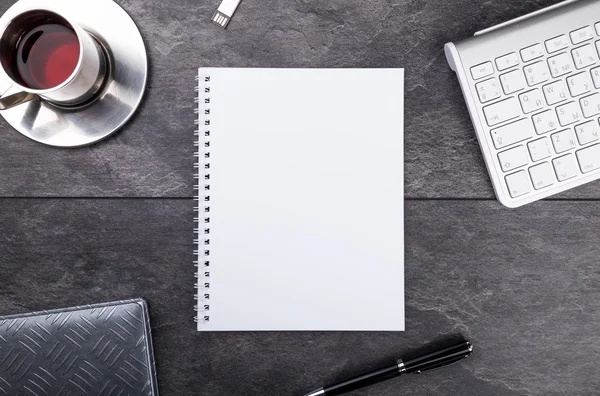 Kladblok, pen, thee en toetsenbord op stenen tafel — Stockfoto