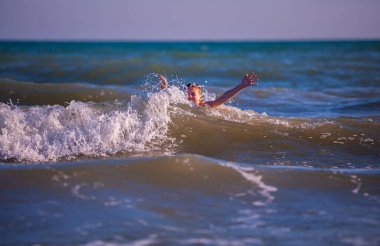 Sahildeki çocuk, yaz zamanı dalgalarla oynuyor. Rahatlama ve sağlıklı bir yaşam anlayışı.