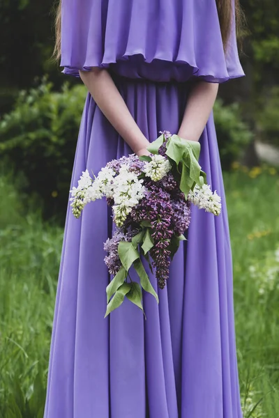 Lilac bouquet. A girl in a lilac dress holds a bouquet of lilacs of different shades in her hands
