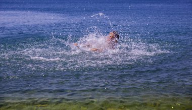 Sahilde dalgalarla oynayan bir çocuk, yaz zamanı. Denizde yaz tatili. Rahatlama ve sağlıklı yaşam tarzı kavramı