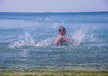Sahilde dalgalarla oynayan bir çocuk. Denizde yaz tatili. Rahatlama ve sağlıklı yaşam tarzı kavramı