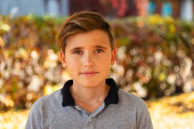 Güneşli bir günde, sonbahar parkında kameraya bakan bir çocuğun portresi. Mutlu çocukluk yaşam tarzı konsepti