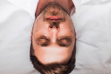 Sakallı ve gözlerinin altında altın bantlarla rahatlayan genç yakışıklı bir adam portresi. Üst görünüm