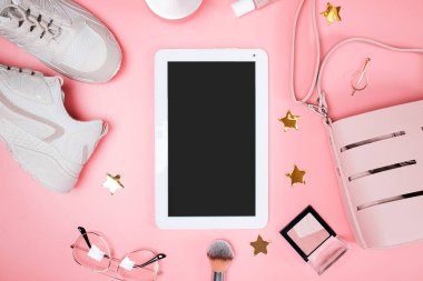 Pembe arka planda kadın aksesuarları ve makyaj aletleriyle tablet maketi, üst görünüm. Moda düzlüğü