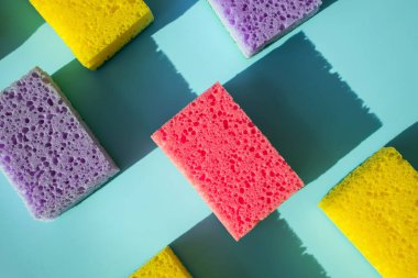 Mavi arka planda bulaşık yıkamak için sünger temizliyorum. Doğal ışıkta, sert gölgelerle. Temizlik hizmeti kavramı