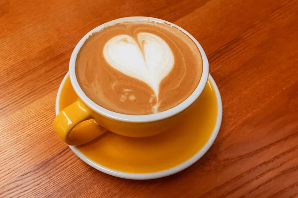 Желтая чашка кофе с искусством латте в форме сердца — стоковое фото
