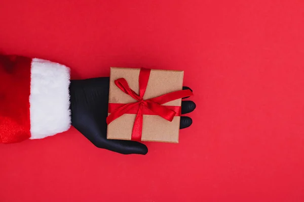 Hand in beschermende handschoen houdt een rode geschenkdoos met een lint — Stockfoto