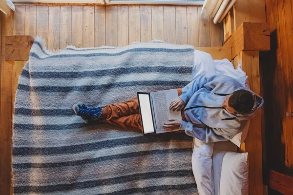 Uomo che lavora su laptop seduto su un letto accogliente — Foto Stock