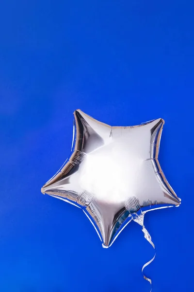 Eine silberne Glitzerfolie sternförmiger Ballon auf blauem Grund — Stockfoto