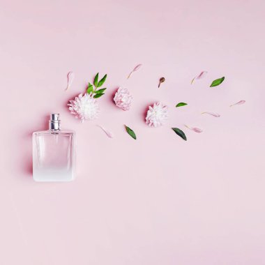 Pembe arka planda bir şişe parfüm, çiçekler ve yapraklar..