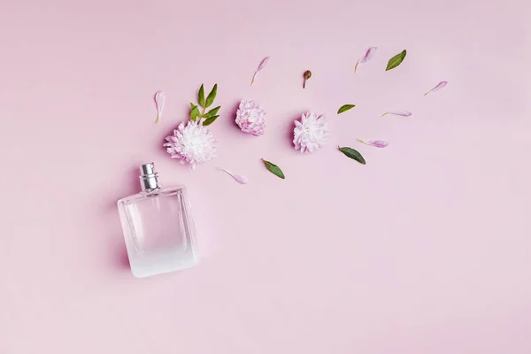 Бутылка духов, цветов и лепестков на розовом фоне. — стоковое фото