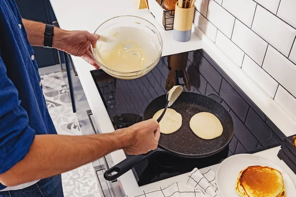 Чоловік смажить млинці на сковороді на своїй кухні . — стокове фото