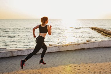 Genç bayan deniz kenarında koşuyor.