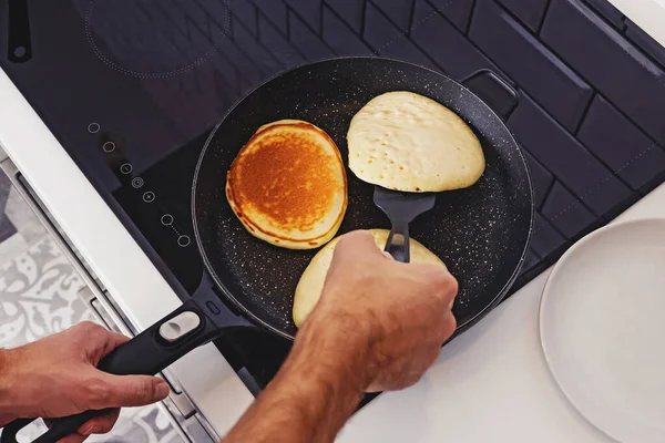 Homem fritando panquecas na panela em sua cozinha. — Fotografia de Stock