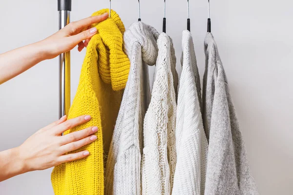 Mani delle donne che scelgono maglione a maglia gialla tra gli altri su appendiabiti — Foto Stock