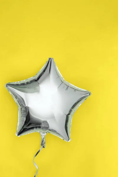 A silver glitter foil star shaped balloon isolated on bright yellow background. Illuminating and ultimate gray colors of the year 2021
