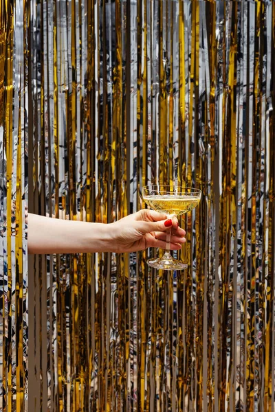 Ręka trzyma kieliszek szampana na tle błyszczącej metalowej kurtyny — Zdjęcie stockowe