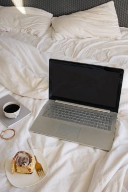 Boş ekranlı dizüstü bilgisayar tarçınlı çörek ve yanan mum.