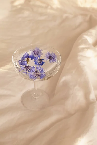Blue flower heads in a glass with clear water standing on the bed — Stock Photo, Image