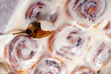 Lezzetli ev yapımı taze tarçınlı ruloların üzerinde kaşık var.