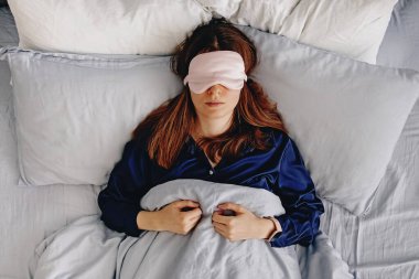 İpek giysili genç bir kadın, gözleri maskeyle kaplı bir yatakta uyuyor..