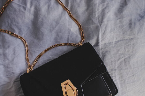 Black womans small bag with chain on the bed