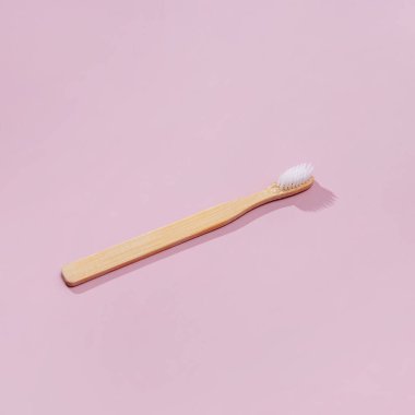 Pembe arka planda gölgeleri olan tahta diş fırçası.