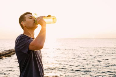 Genç erkek koşucu koşudan sonra şişeden su içiyor.