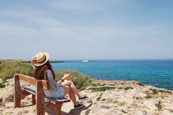 Mulher de chapéu de palha sentado no banco perto do mar. — Fotografia de Stock