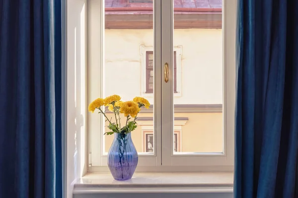 Yellow flowers in a glass blue vase on a windowsill — Stock Photo, Image