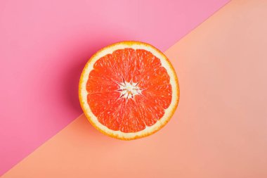 Turuncu ve pembe arkaplanlı greyfurtun yarısı.