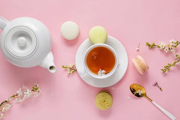 Macarrones, té y flor sobre fondo rosa. — Foto de Stock