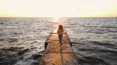 Denizde taş iskelede yeni güne doğru koşan genç bir kadının yavaş çekim sahnesi.