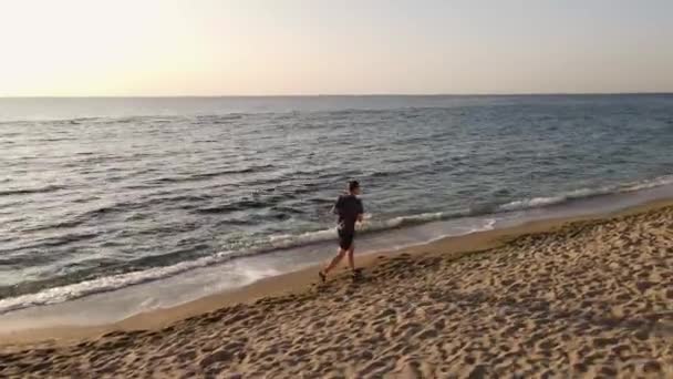 Tiro aéreo de um jovem correndo em uma praia de areia — Vídeo de Stock