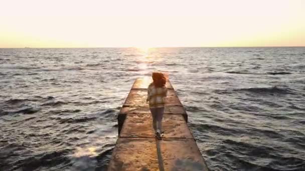 Slow motion shot van jonge vrouw loopt op stenen pier in de zee naar nieuwe dag — Stockvideo